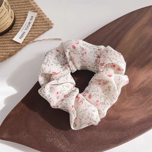 Minimalist cream floral scrunchie with pink flower pattern on a wooden display board