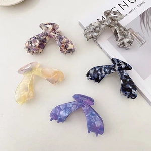 Flat lay of five large marbled acetate hair claws in various colors with a magazine