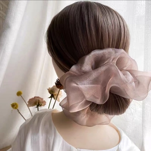 Détail d'un chouchou élégant en organza rose champagne sur des cheveux foncés