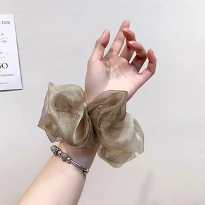 Chouchou géant en organza doré brillant porté au poignet sur fond minimaliste