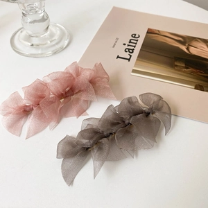Detail of multi-layered organza bow hair clips in soft pink and taupe on a white table