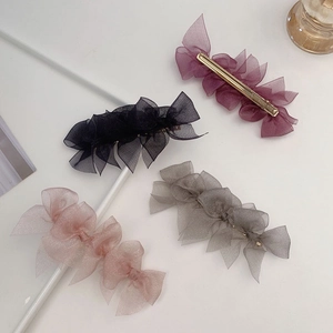 Detail of four organza bow hair clips in purple, black, pink and grey with gold metal clips
