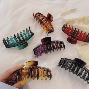 Grandes pinces à cheveux en résine en cinq couleurs dont ambre et vert sur tissu blanc