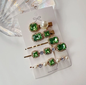 Close-up of 5-piece emerald rhinestone and pearl hair clip set on a white display card
