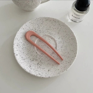 Detailed close-up of matte pink U-shaped hair fork on a white ceramic dish