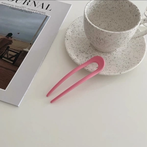 Macro detail of a minimalist pink matte U-shaped hair pin against ceramic decor