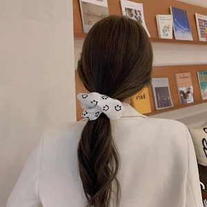 White satin scrunchie with smiley face pattern worn on a low ponytail with a white suit