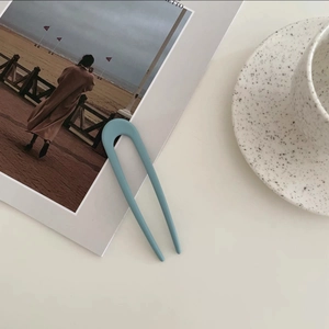 Detail of matte blue U-shaped hair pin for women on a stylish aesthetic magazine background