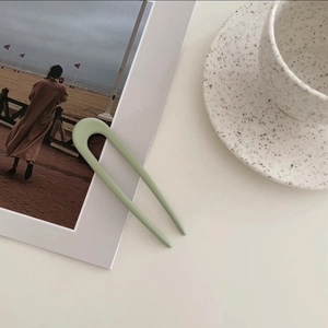 Close-up of matte mint green U-shaped hair pin on white table with lifestyle props