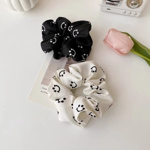 Detailed shot of black and white silk scrunchies with smiley face patterns and satin finish