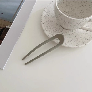 Detail view of a matte dark grey U-shaped hair pin on a minimalist ceramic table
