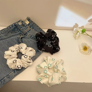 Detailed view of three satin smiley face scrunchies in black, white, and blue colors