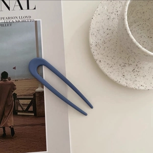 Detail view of a matte blue U-shaped hairpin set against elegant lifestyle props