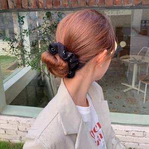 Détail d'un chouchou noir avec motifs smiley blancs sur un chignon bas pour femme