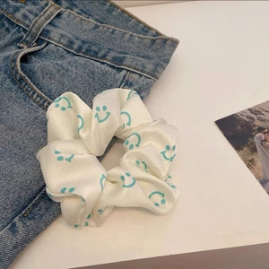 Close-up of dual-tone scrunchie with blue smiley faces on cream satin fabric surface