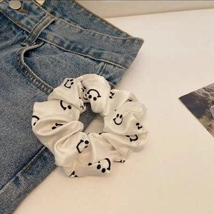 Detail of a white satin scrunchie with smiley face print on denim jeans surface