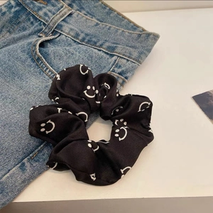 Detail of black satin scrunchie with white smiley face prints on denim background