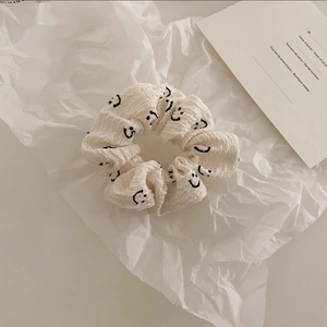 Détail du chouchou en coton blanc avec broderie smiley noir sur fond de papier