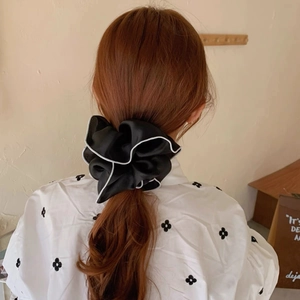 Detail of a large black mesh scrunchie with white trim styled on a low ponytail