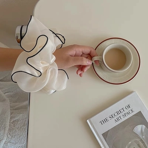Detail showing oversized cream organza scrunchie with black trim on wrist with soft lighting