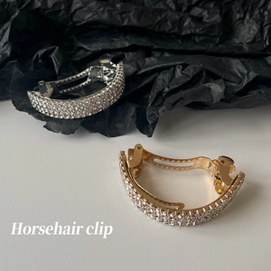 Detail der gebogenen Pferdeschwanz-Clip mit Reihen funkelnder weißer Strasssteine in Gold
