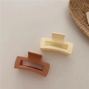 Detail of large matte square hair claws in cream and caramel colors with hollow design