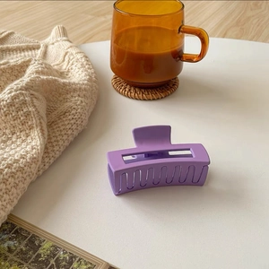 Detail of matte purple rectangular hair claw clip with cutout design on beige fabric
