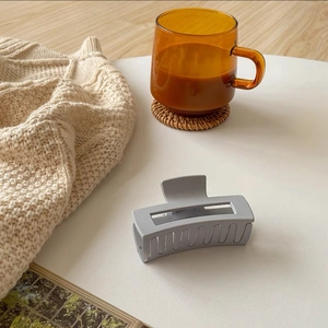 Matte grey rectangular claw clip shown on a white table with cozy lifestyle props
