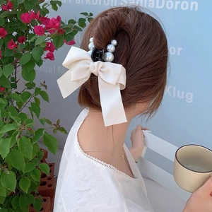 Detail of silk bow hair claw clip with pearls worn by a model in a garden setting