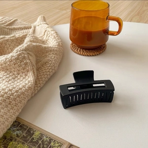 Detailed macro view of a large matte black rectangular hollow hair claw clip on knitwear