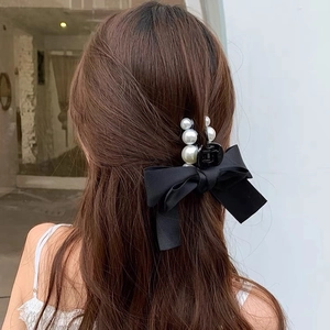 Elegant black bow hair claw with gradient pearls shown on long brown hair back view