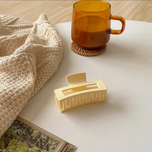 Close-up of a matte cream yellow rectangular hair claw clip on a cozy white desk