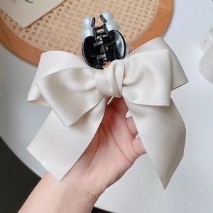 Detail of elegant cream satin bow hair claw clip featuring refined faux pearl embellishments