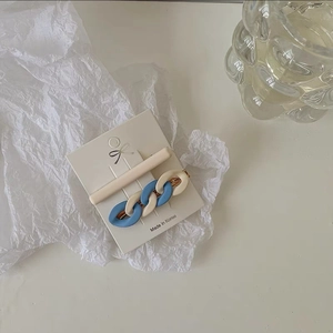 Detail view of interlocking chain hair clip and matte beige barrette on a display card