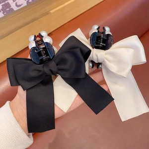 Detail of satin bow hair claws in black and beige with elegant pearl decorations