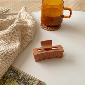 Macro detail of a rectangular matte hair claw clip in a warm vintage brick red color