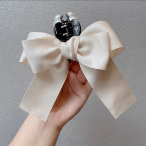Close-up of elegant cream satin bow hair claw clip featuring white pearl decorations