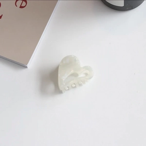 Macro shot of a cream-white heart-shaped acetate hair claw clip with pearlescent marble texture