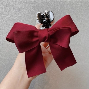 Detail of burgundy bow hair claw with pearl accents showing texture and hand-held scale