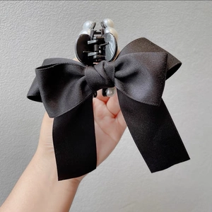 Detail showing a black satin bow hair claw clip with white faux pearls on a neutral background