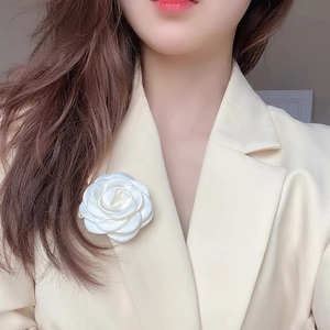 Detail of white satin camellia flower hair clip accessory worn on a beige blazer lapel