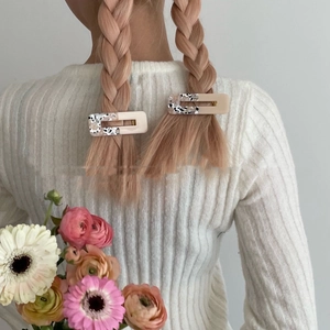 Detail of marble pattern resin hair clips worn on pink braided hair with floral background