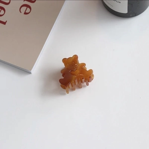 Detail of a brown amber bear-shaped acetate hair claw clip with a relief heart on white