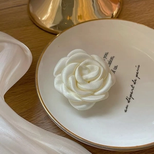 Close-up of white satin camellia hair clip featuring layered petals and a silky texture