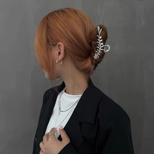 Detail view of large silver metal fishbone hair claw clip with minimalist cross necklace