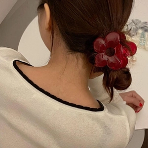 Detail showing a red translucent flower claw clip styled on a woman's hair bun