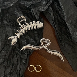 Close-up of silver metal shark clips and golden hoop earrings on a dark textured background