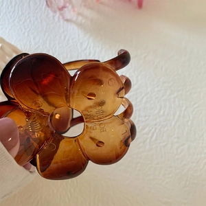 Macro shot of large translucent amber flower hair claw with metal spring and logo detail