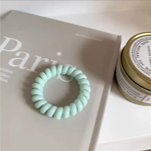 Detailaufnahme eines minzgrünen Spiral-Haargummis auf einem Magazin im Lifestyle-Stil