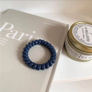 Nahaufnahme eines dunkelblauen Spiral-Haargummis auf einem Magazin neben einer Kerze